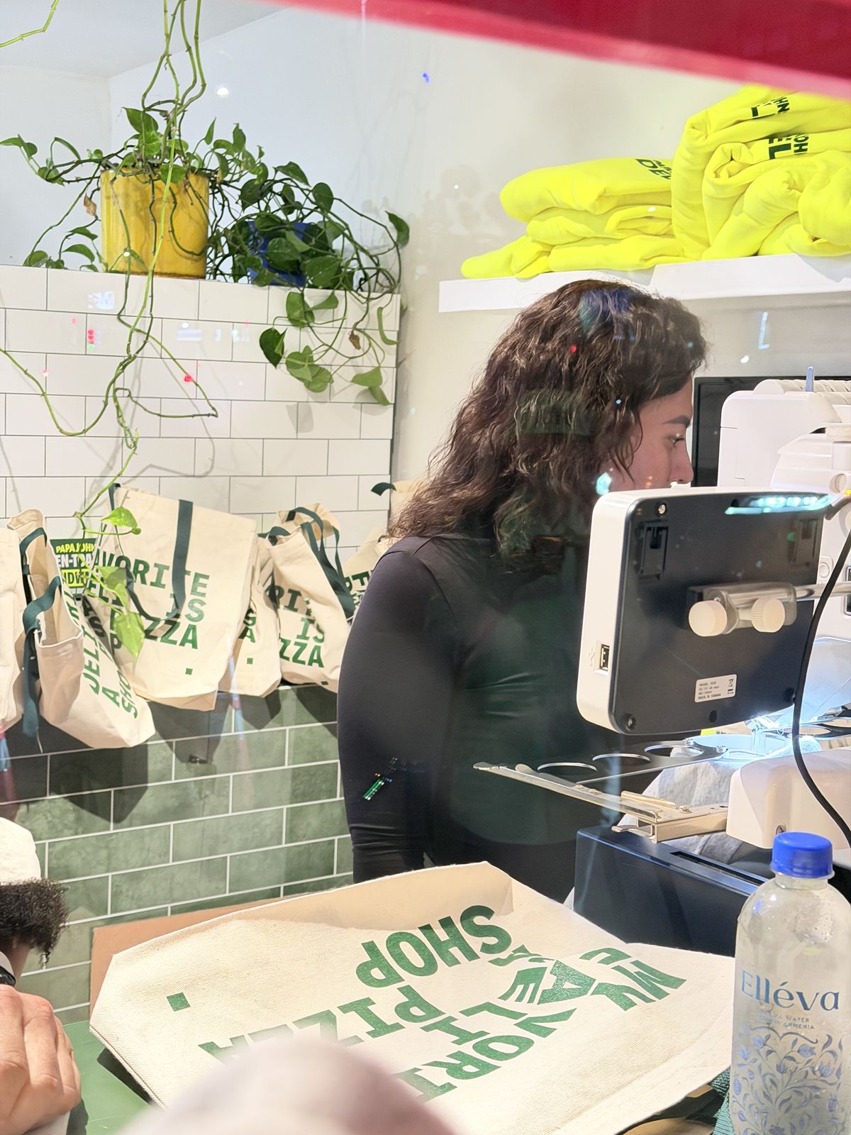 Printer heat-pressing custom canvas tote bags at an event counter with finished totes hanging behind